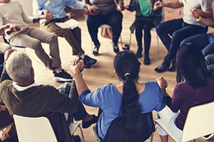 Group of people sitting in chairs in a circle holding hands